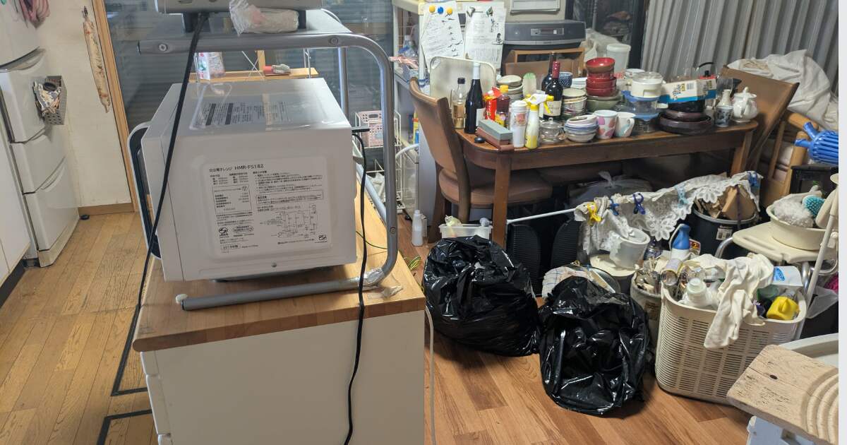 不用品回収前のダイニングとキッチンに食器や家電、日用品が多く置かれている様子