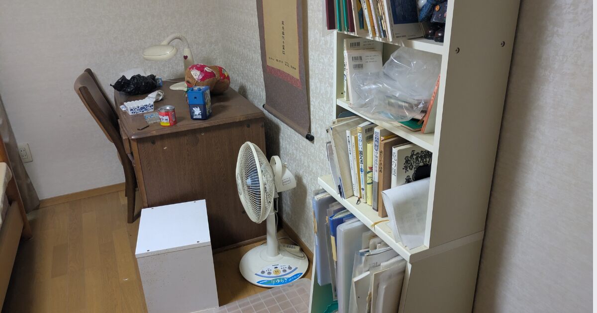 不用品回収前の部屋に本棚や机、扇風機、書類などが残っている様子